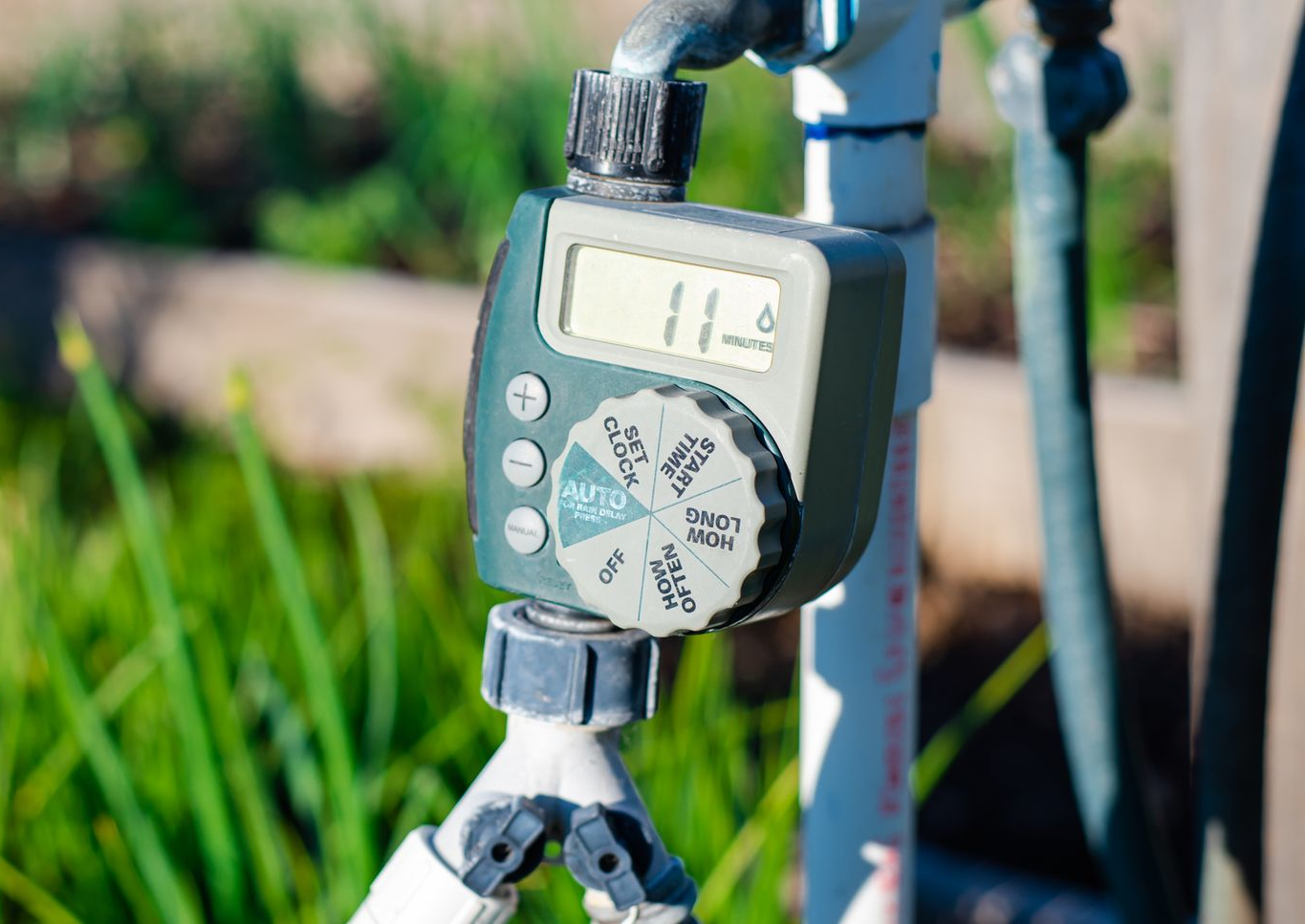 A digital water timer connected to a faucet in a garden setting.