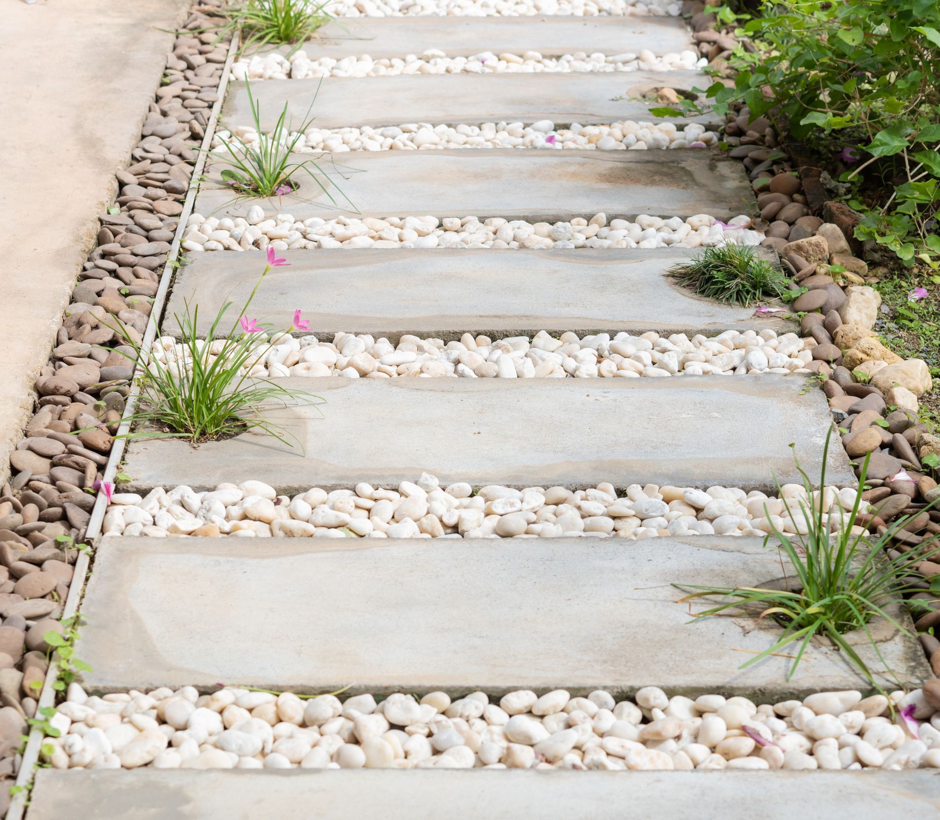 Stone walkway with concrete slabs, white pebbles, and green grass.