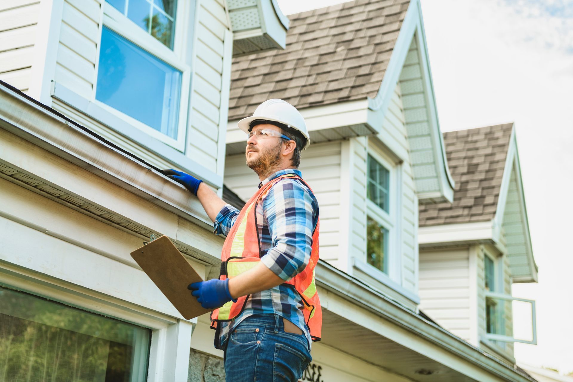 A man in a hard hat is standing in front of a house holding a clipboard.