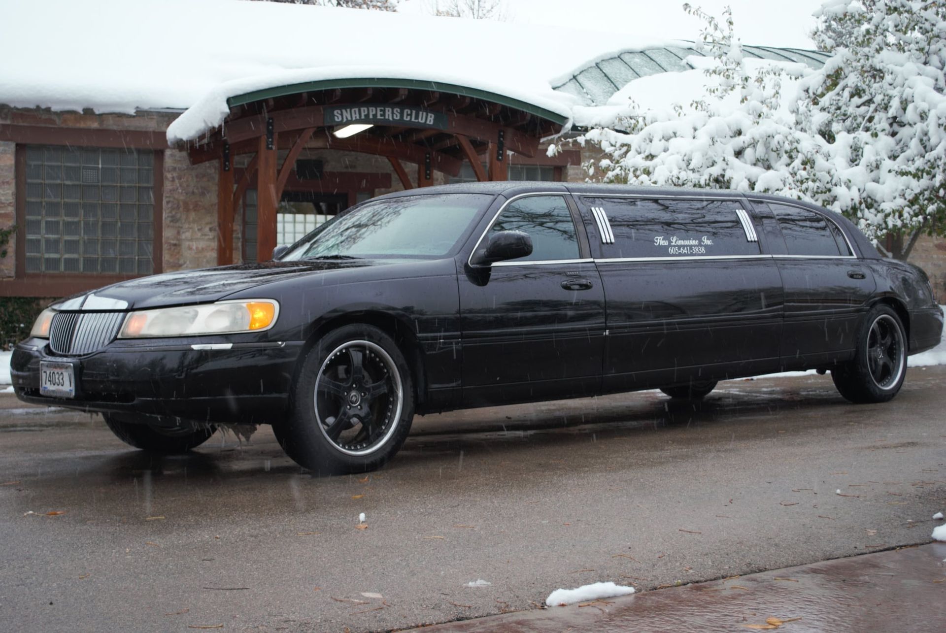 Black limousine parked in front of a building with snow on the roof and trees.