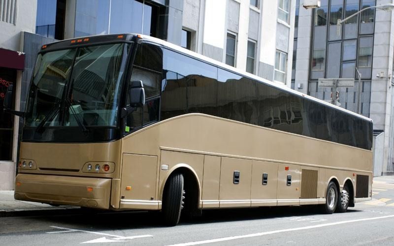 Tan tour bus parked on a city street in front of a building.