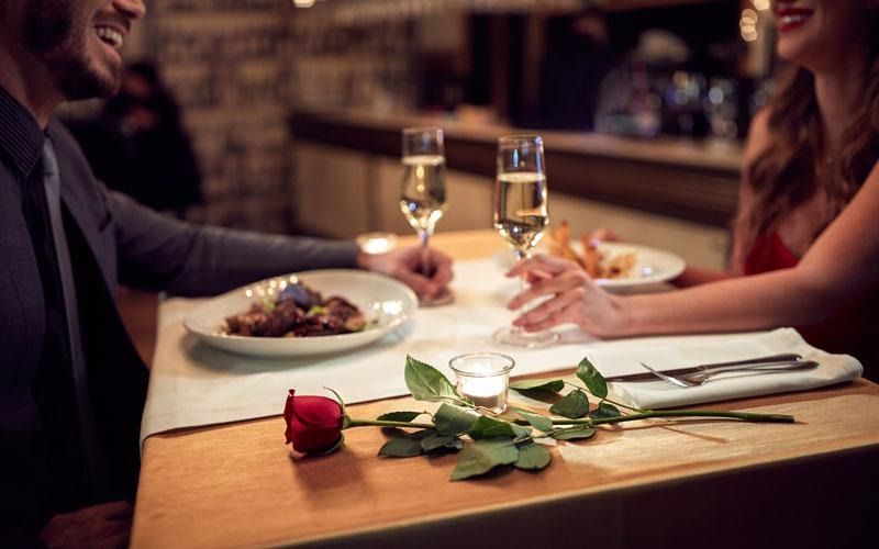A couple on a date, toasting champagne, with food and rose on the table.