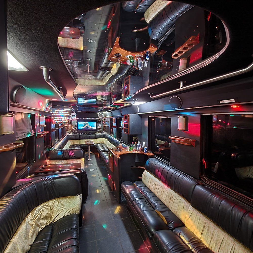 Interior of a party bus with black leather seating, disco lights, mirrored ceiling, and bar.