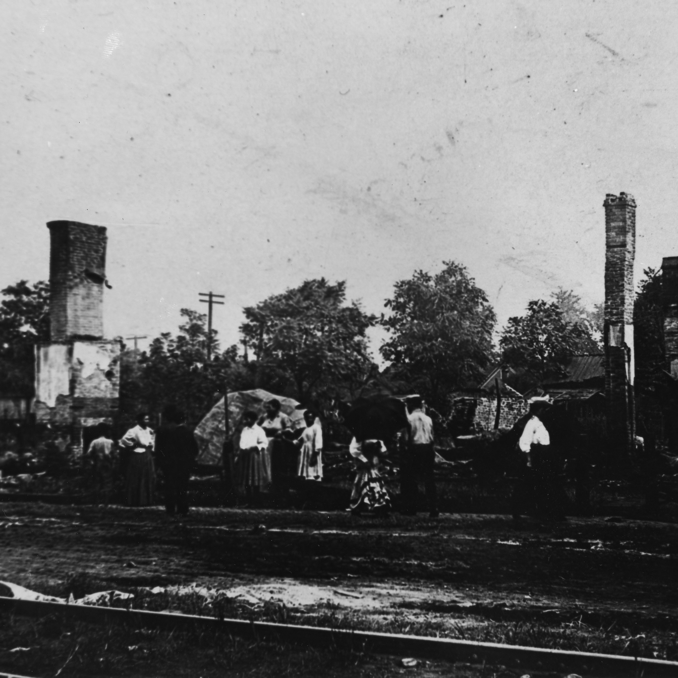 Black and white photograph of black individuals standing near the burned out buildings of their former homes and businesses in Springfield Illinois in 1908.