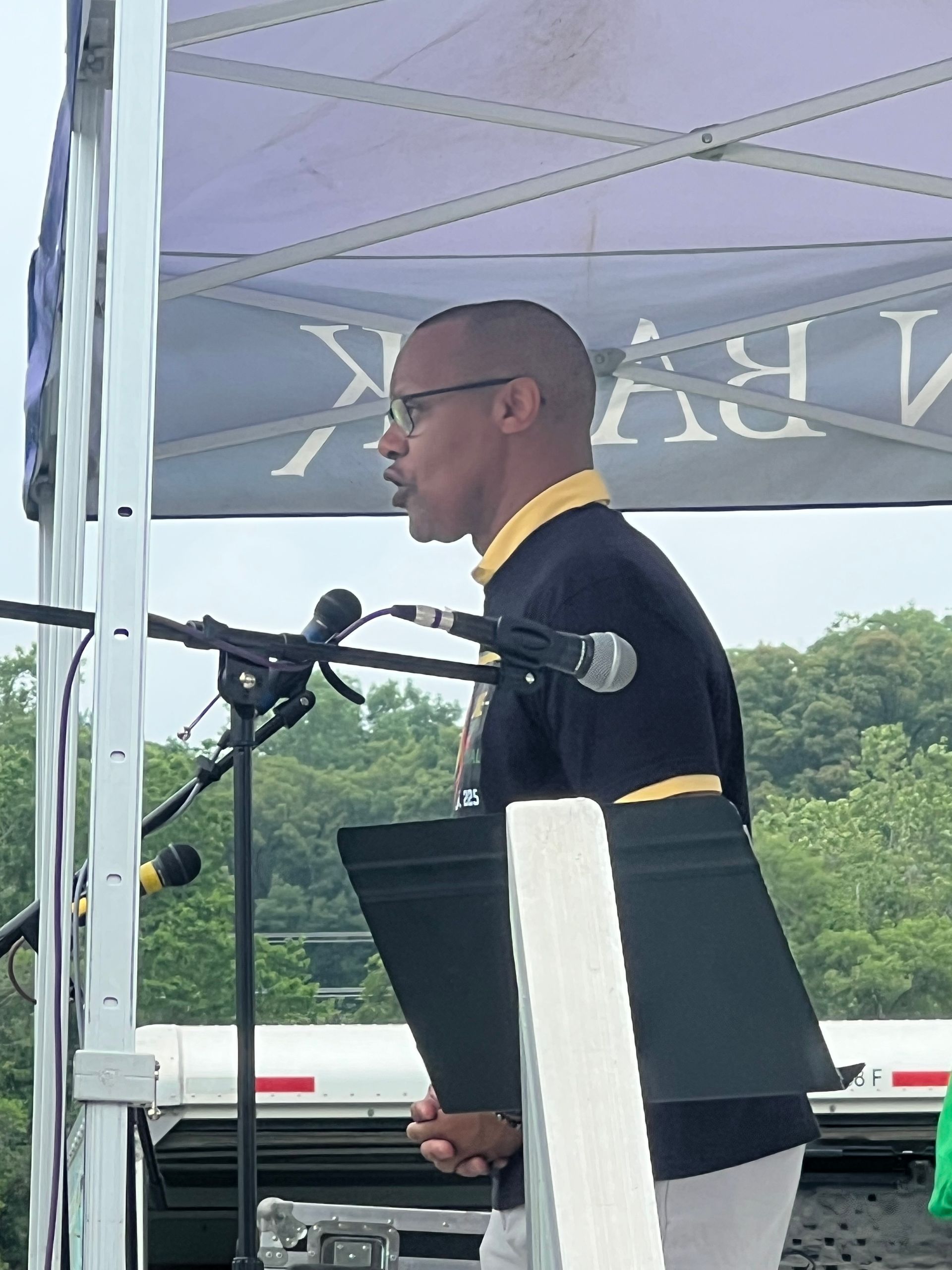 A man is giving a speech in front of a microphone under a tent.