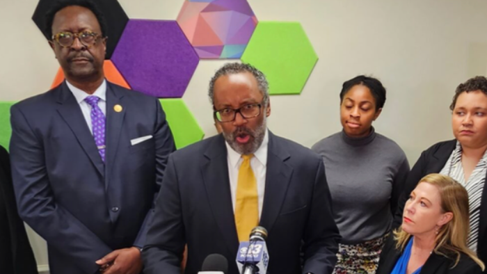 President Nimrod Chapel, Jr. speaks to the press after a court hearing challenging the photo ID requirement in Missouri. Leaders from around the state stand behind him. 