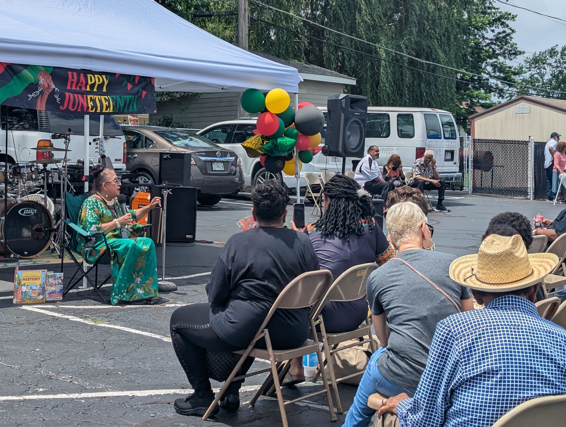 A group of people are sitting in chairs watching a woman tell a story.