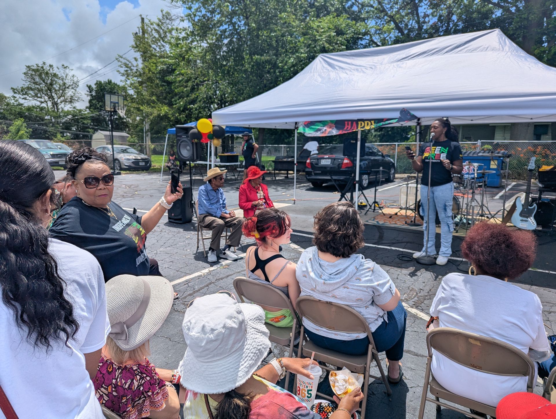 A group of people are sitting under a tent while an older African American couple are receiving an award for their 75th wedding anniversary.