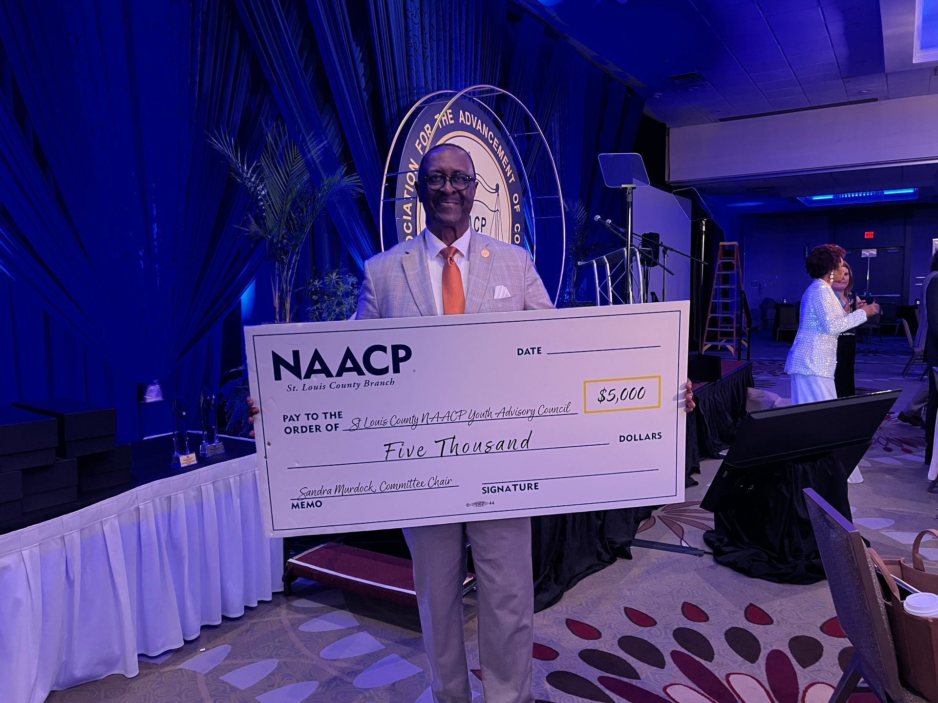 A man in a suit and tie is holding a large naacp check for the St. Louis County Youth Council.