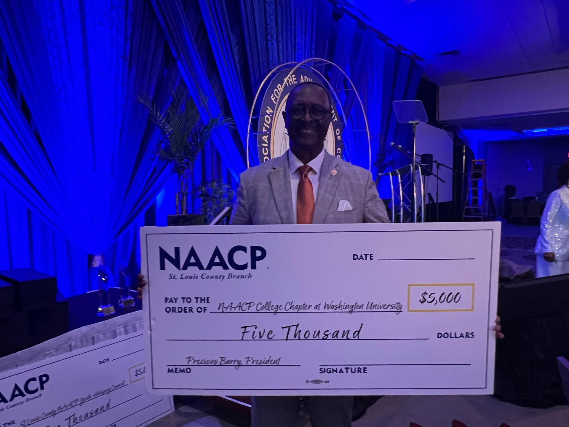 A man in a suit and tie is holding a large naacp check for the Washington University Chapter.