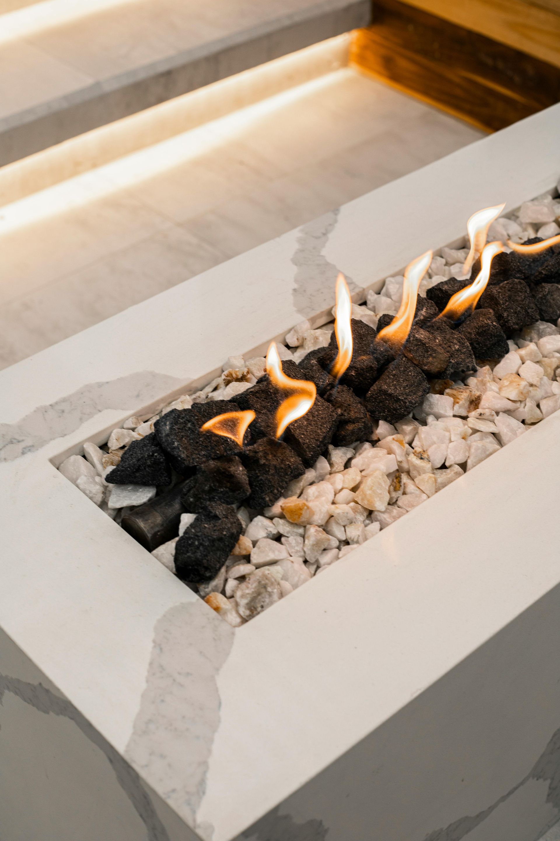 Fire pit with flames, black coals, white rocks, and concrete border.