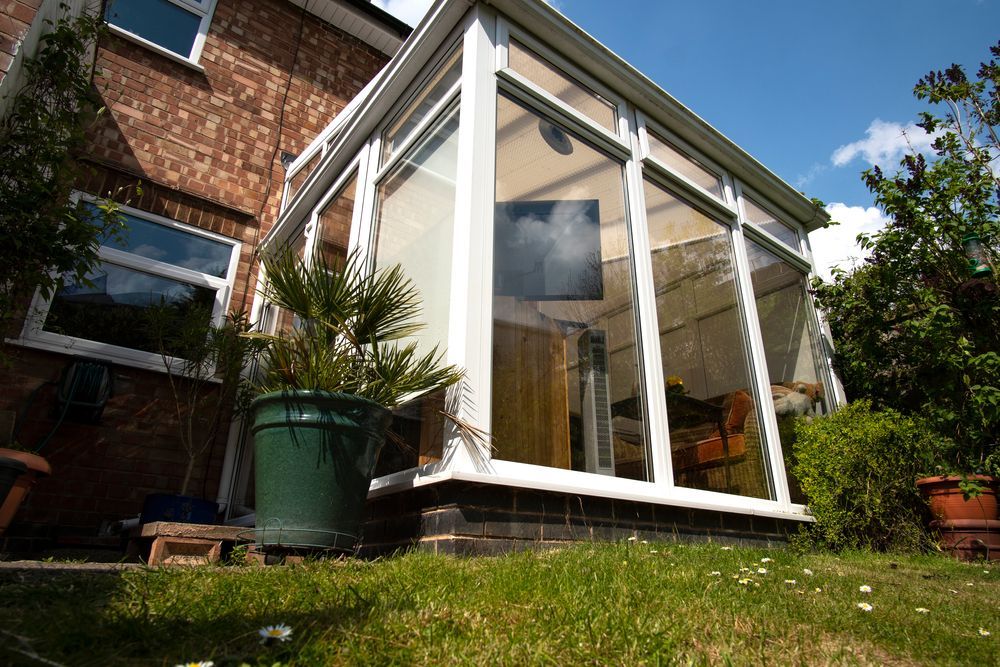 White sunroom conservatory attached to a brick house, with large windows and a grassy garden — Tyrone Building Solutions in Anna Bay, NSW