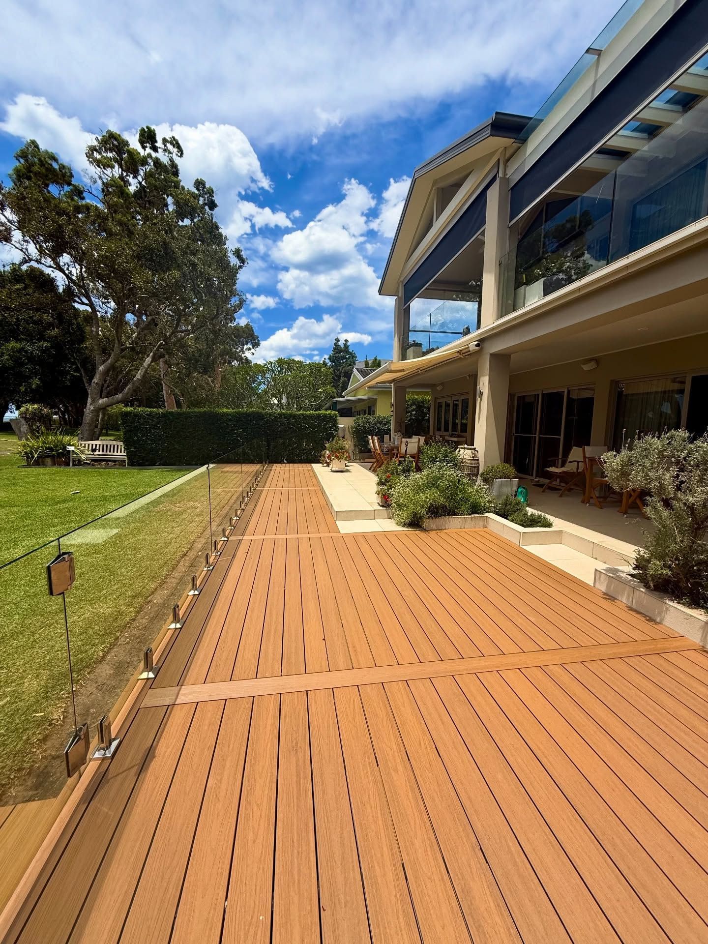 Wooden deck walkway beside a house and garden under a bright blue sky — Tyrone Building Solutions in Anna Bay, NSW