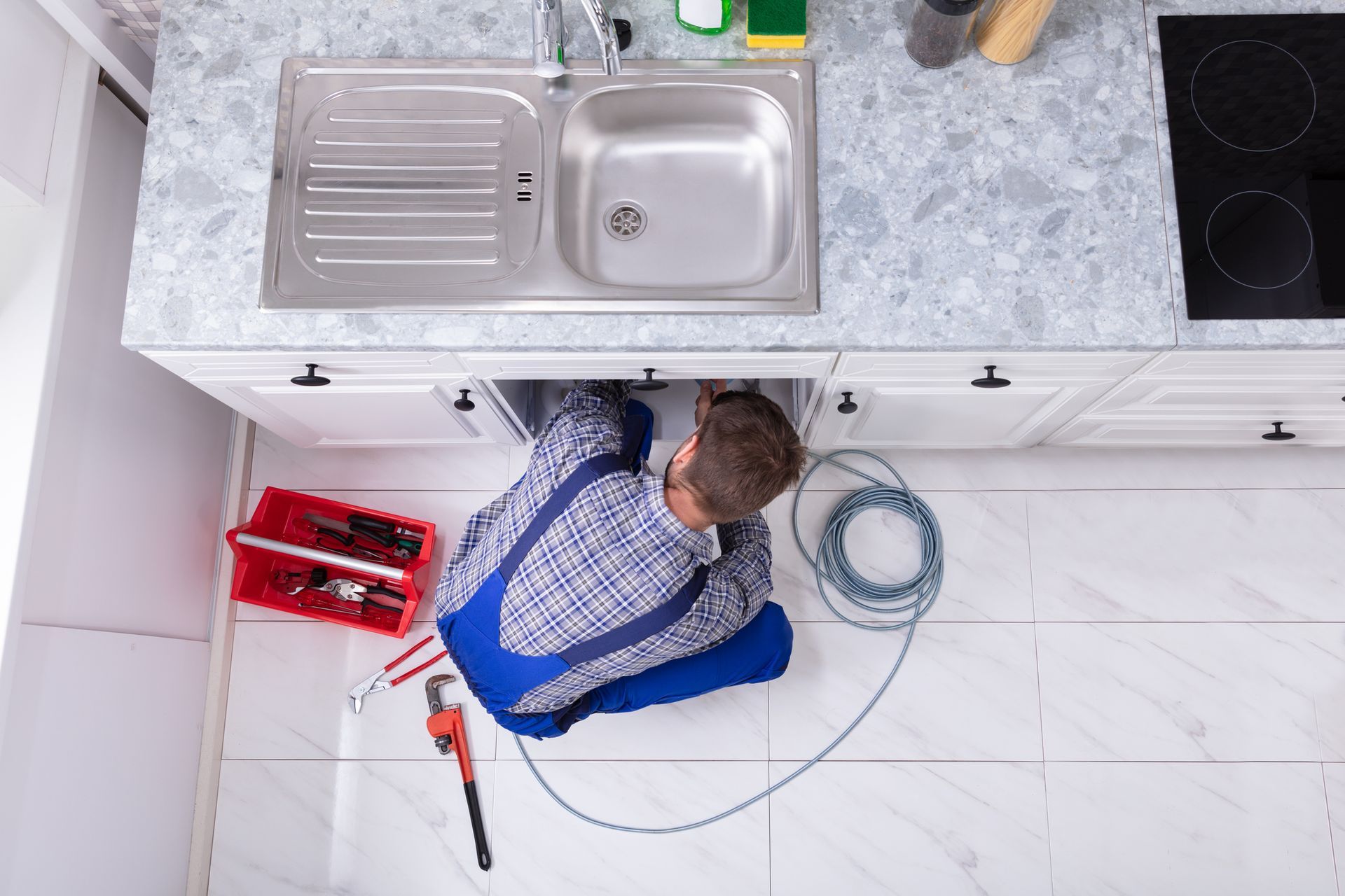 Young male plumber cleaning clogged sink pipe in kitchen providing plumbing service. Young male plumber cleaning clogged sink pipe in kitchen providing plumbing service.