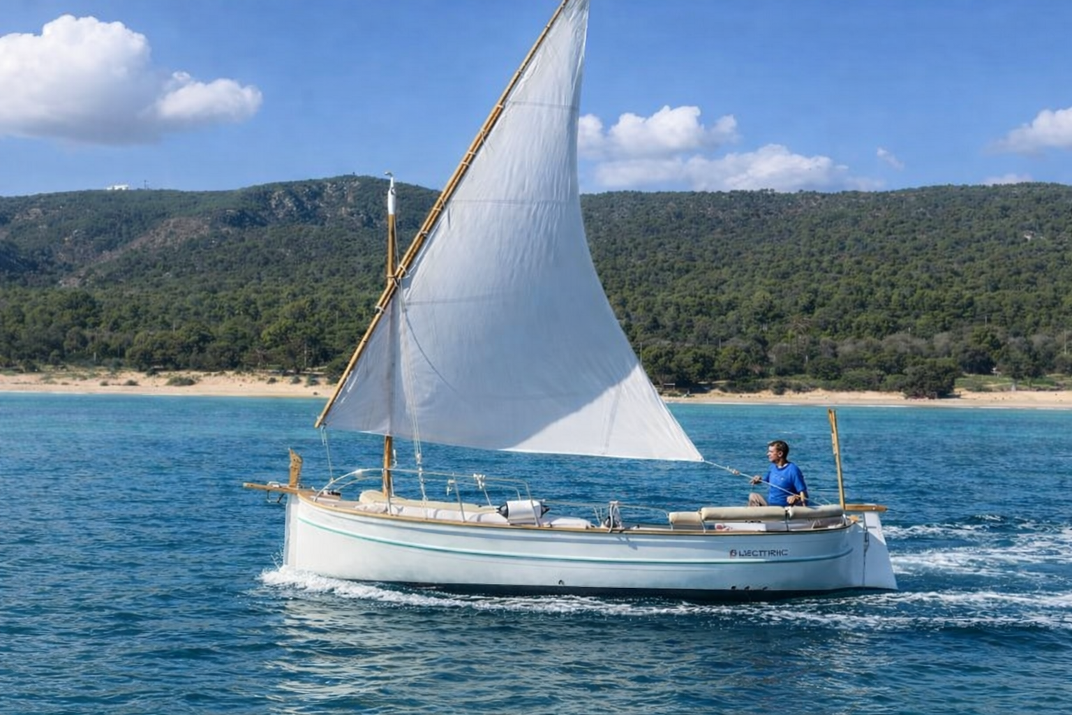 Llaut eléctrico navegando por la costa de Mallorca con vela latina y paisaje mediterráneo de fondo