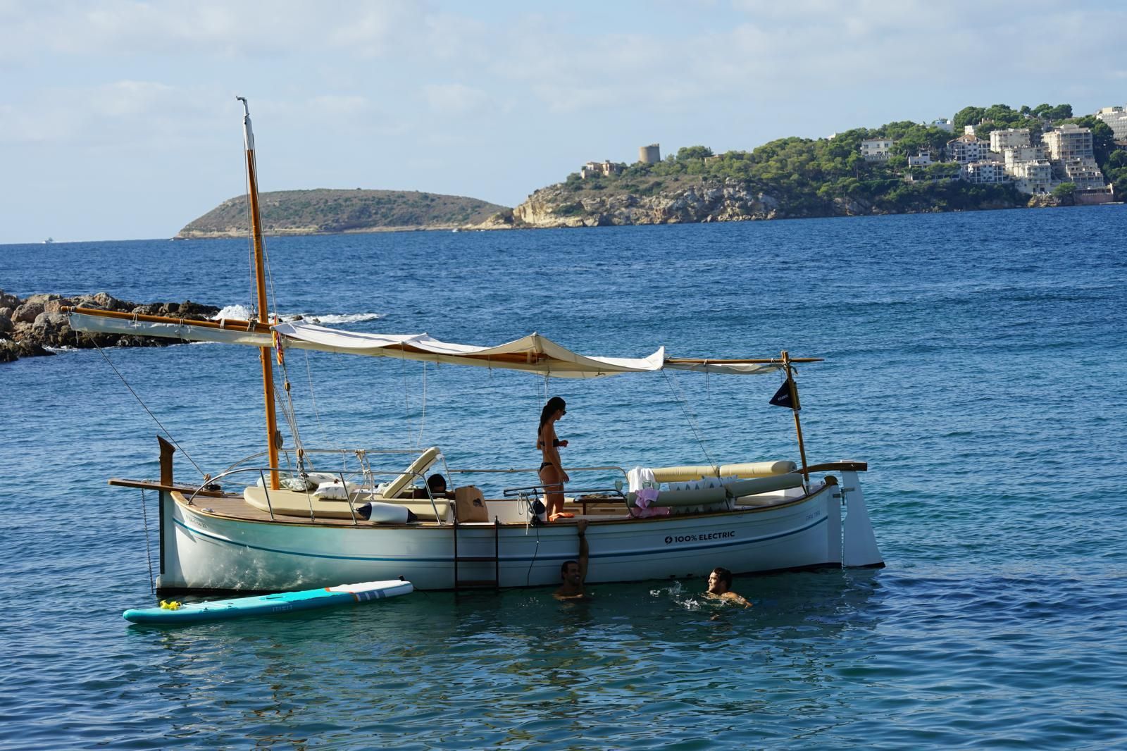 Llauti eléctrico con toldo en aguas azules; persona a bordo, otra nadando.
