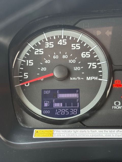A vehicle dashboard showing a speedometer at zero, a fuel level nearly full, a DEF gauge at half, and 128,538 miles.