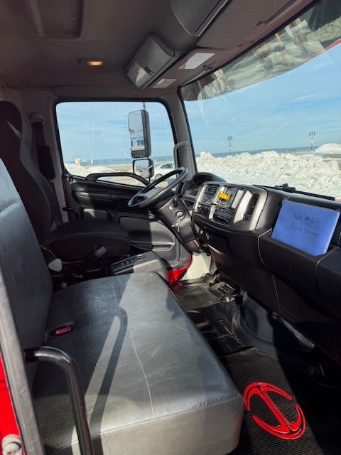 Interior of a truck cab featuring black bench seating, a dashboard with a steering wheel, and a Hino logo on the floor mat.