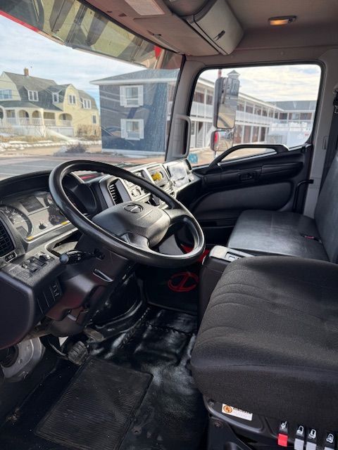 Interior view of a truck cabin with a steering wheel, dashboard, and black seating, overlooking a neighborhood street.
