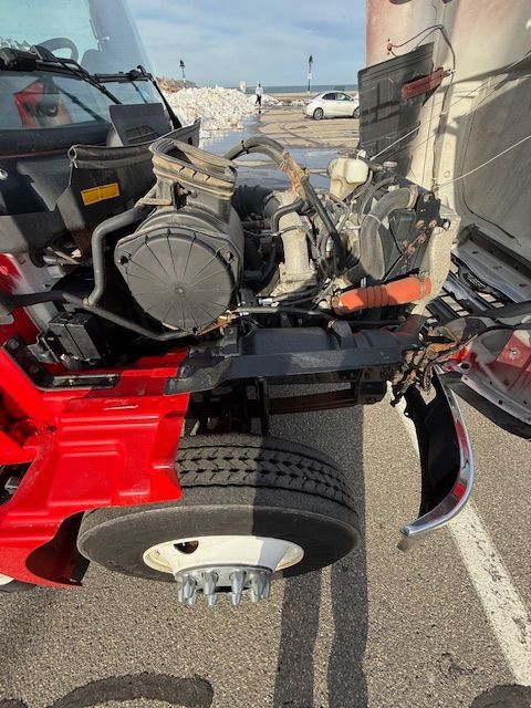 A red semi-truck with its hood tilted forward, exposing the engine components and the front driver-side wheel.