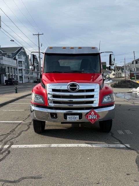 A red Hino commercial truck with a flammable hazardous materials placard parked on a street.
