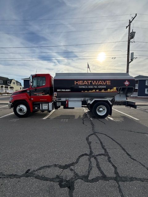 A red Heatwave heating oil delivery truck parked in an asphalt lot on a sunny day.