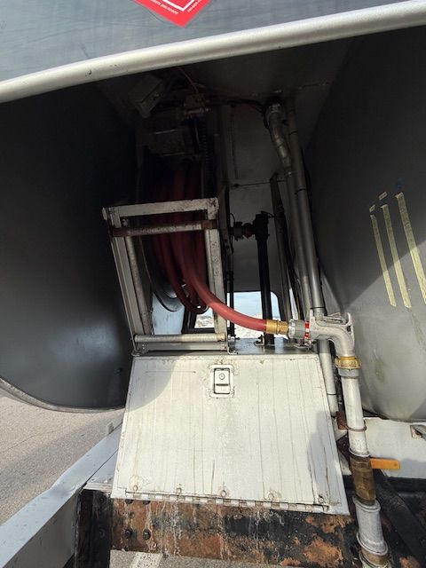 A red delivery hose reel mounted inside a metal compartment on the rear of a fuel tanker truck.