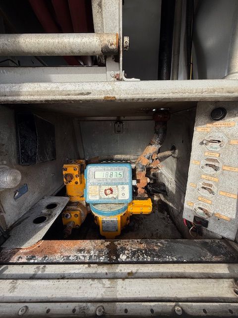 A digital flow meter mounted within a metal storage compartment of a utility truck.