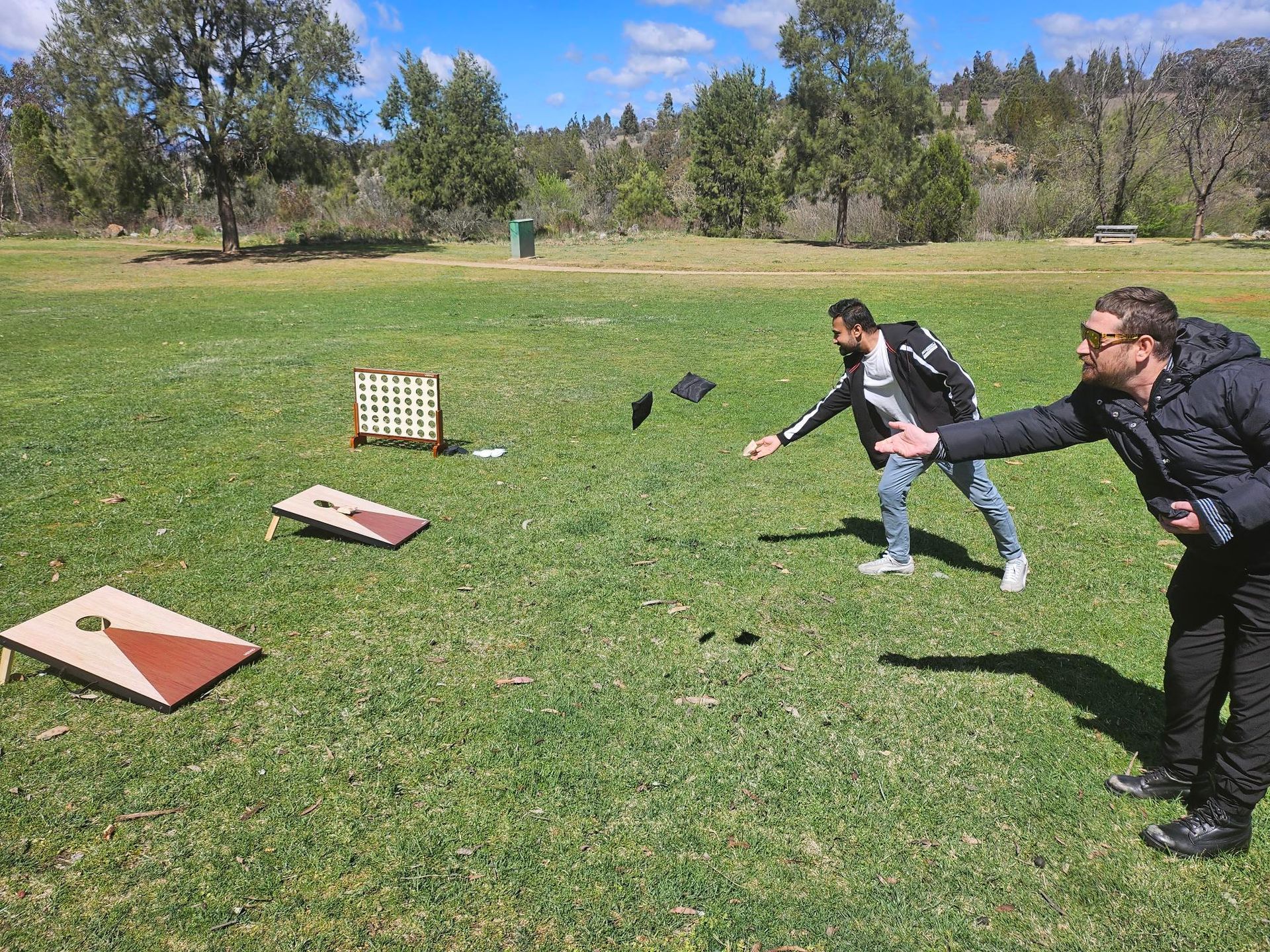 Two men are playing cornhole in a grassy field.