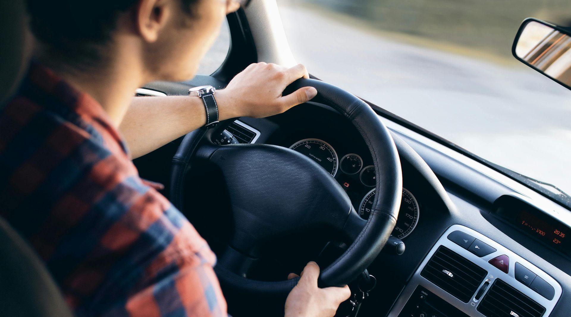 A man in a plaid shirt is driving a car.