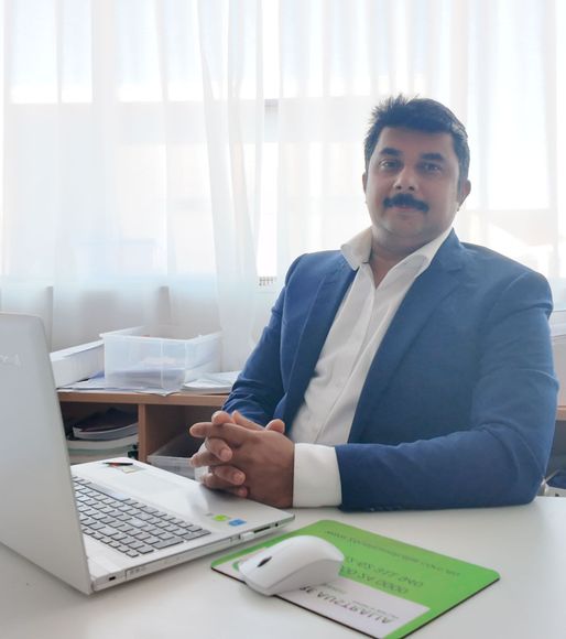 A man in a suit is sitting at a desk with a laptop and a mouse.