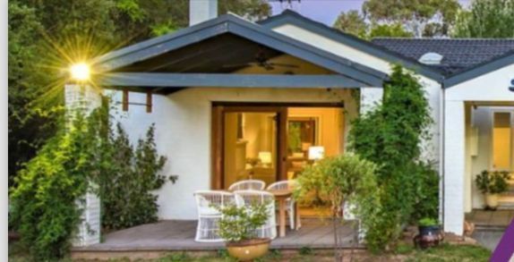 A small white house with a porch and a table and chairs in front of it.
