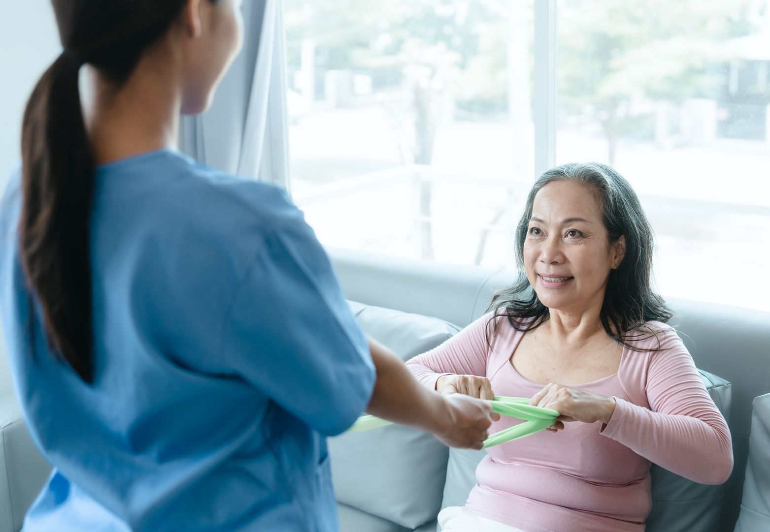 A nurse is holding the hand of an elderly woman sitting on a couch.