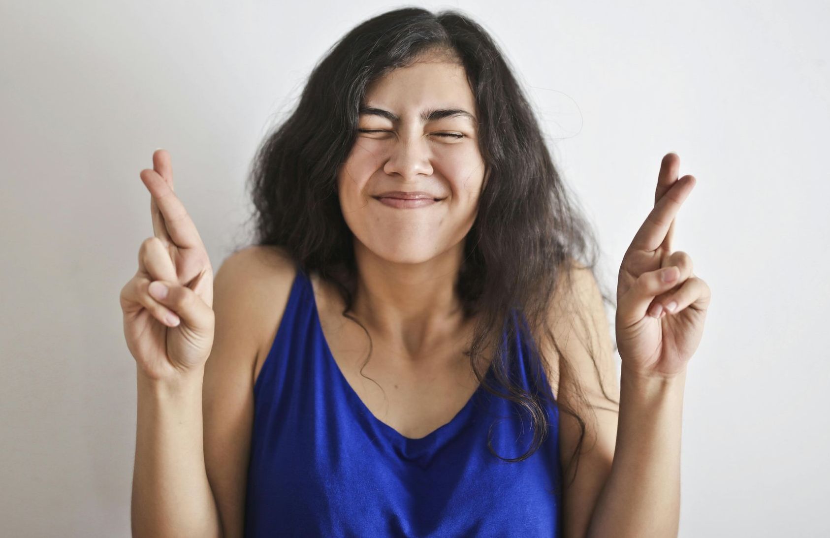 A woman in a blue tank top is crossing her fingers.