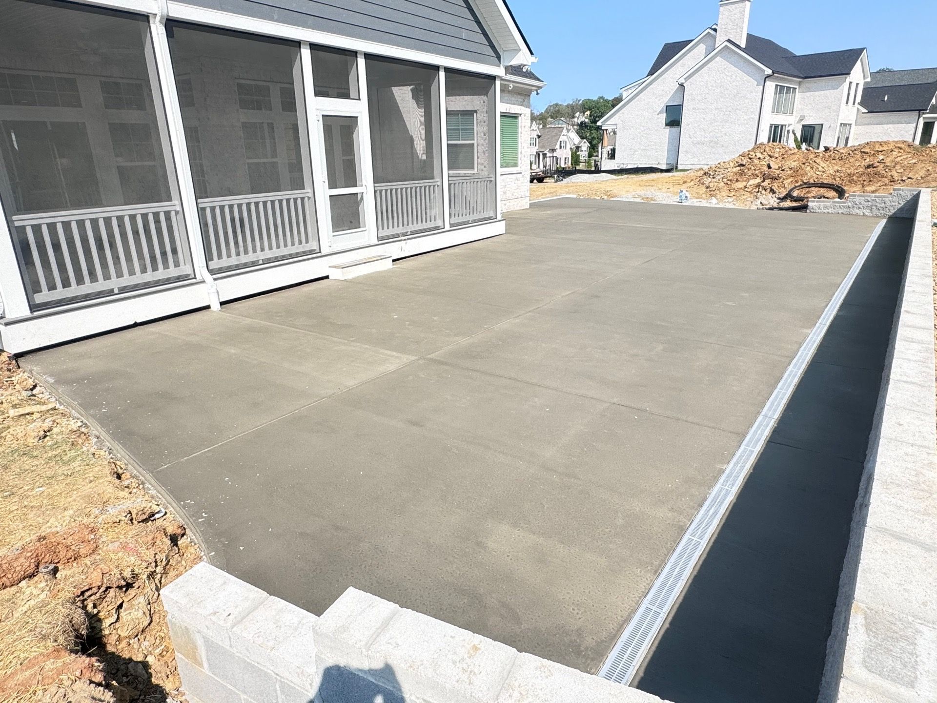 Newly poured concrete patio next to a house with a screened porch and retaining wall.