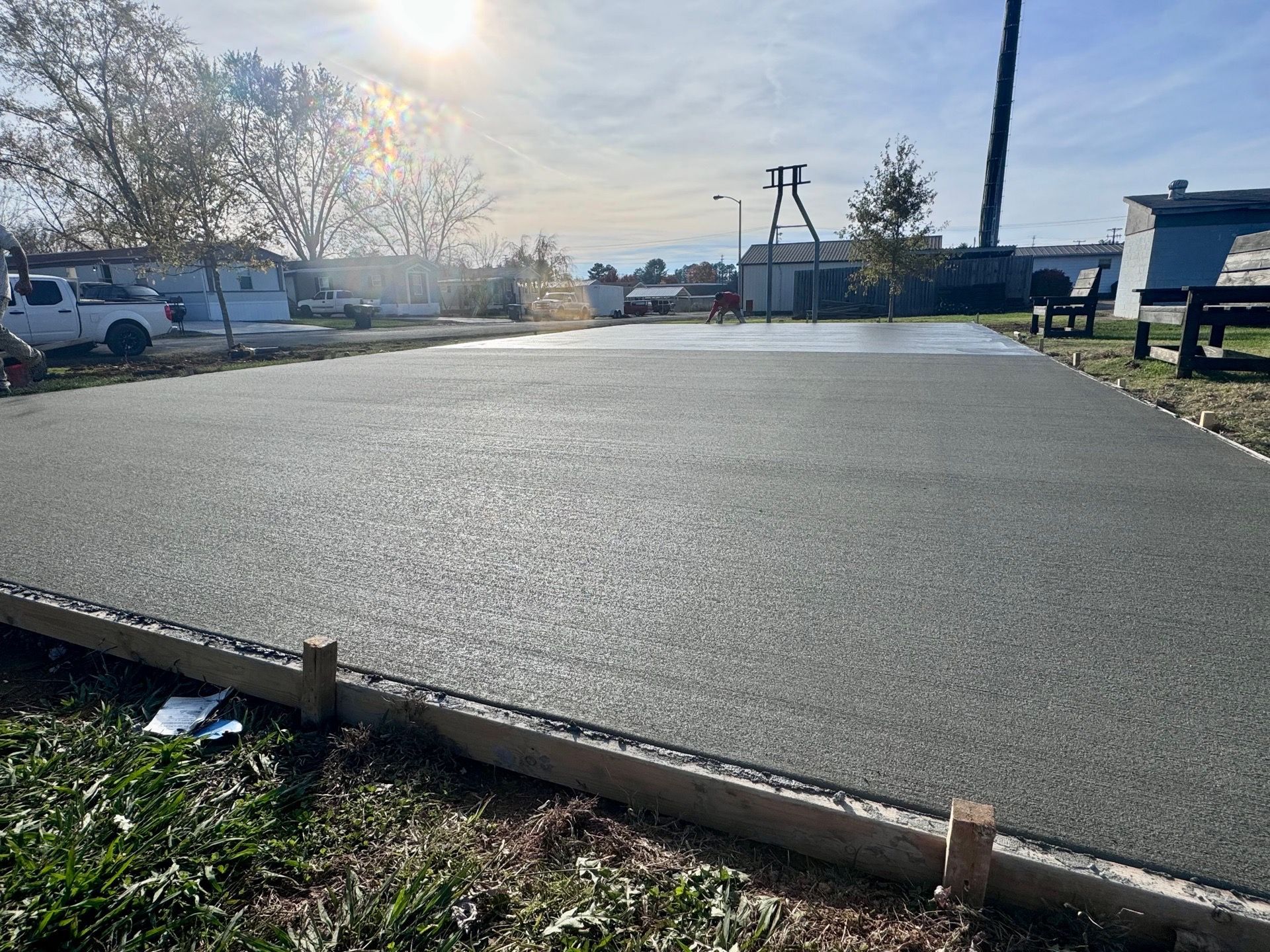 Freshly poured concrete slab outdoors with wooden border, under a sunny sky.