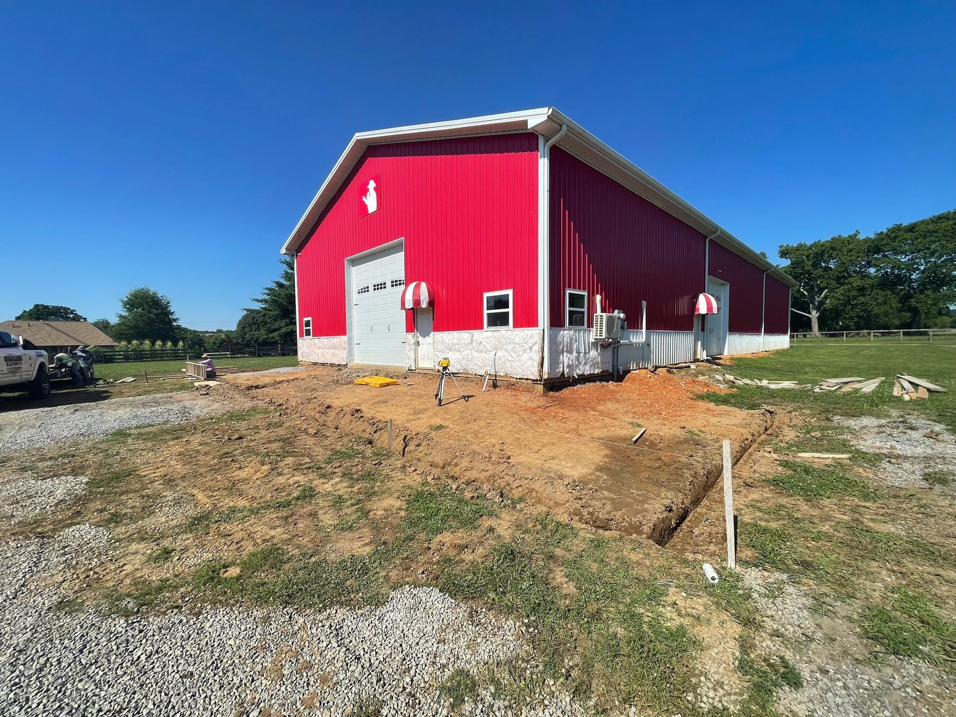 Red barn with white trim, gray garage door, and dirt ground. Blue sky.