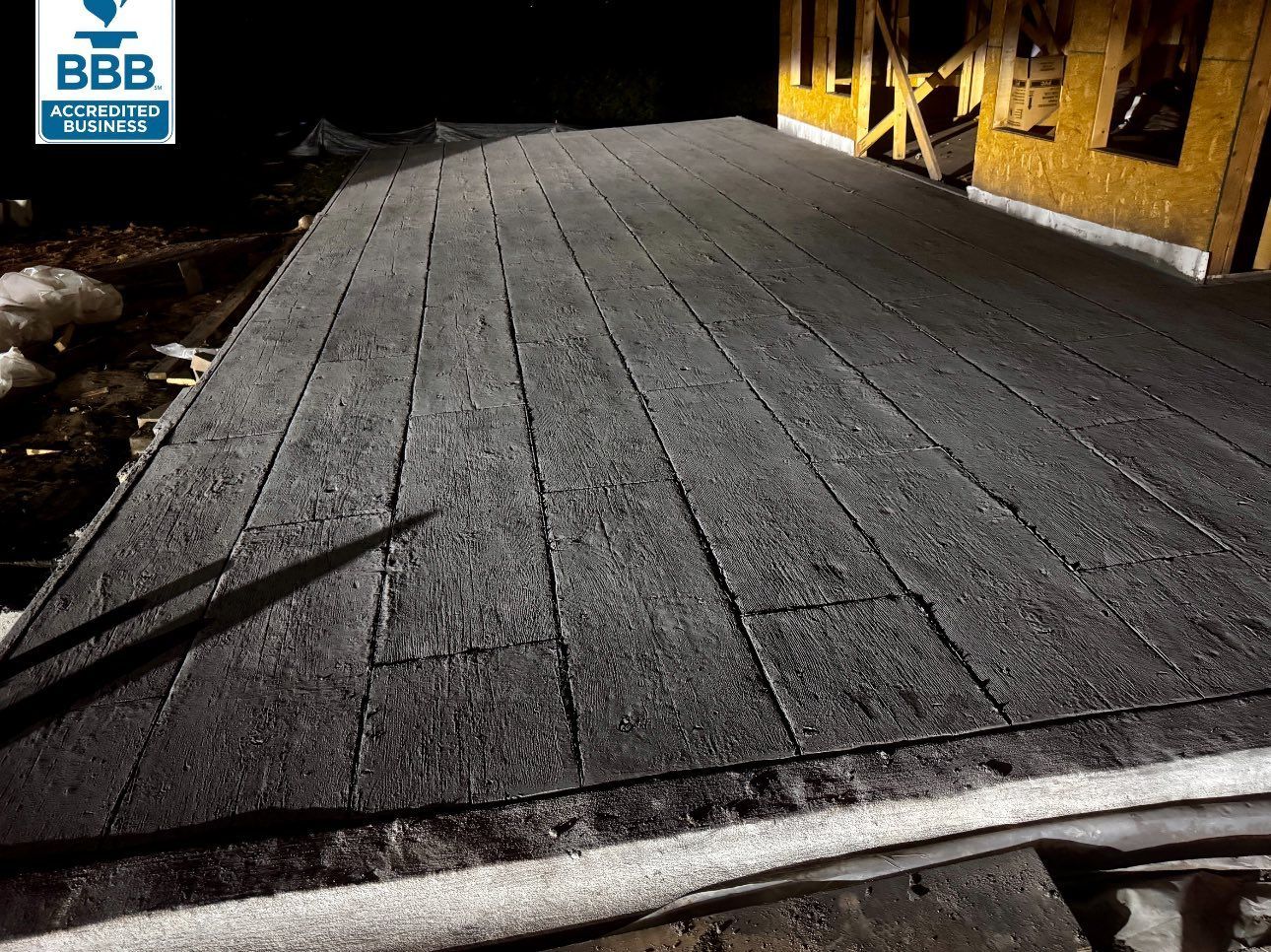 Snow-covered wooden deck next to a building under construction at night, with a Better Business Bureau logo in the top left.