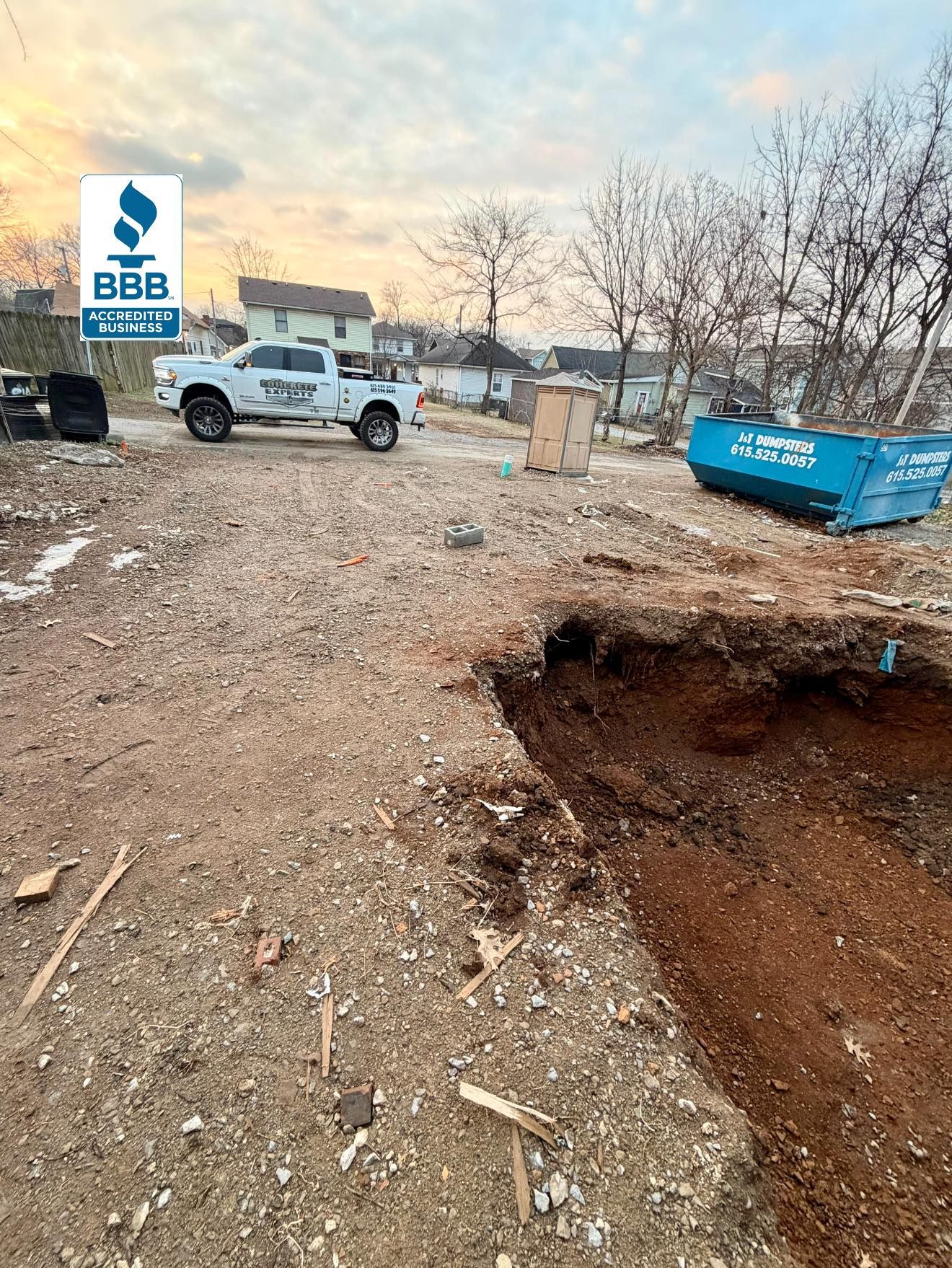 Construction site with a truck, dumpster, and a hole in the ground; sky in background.