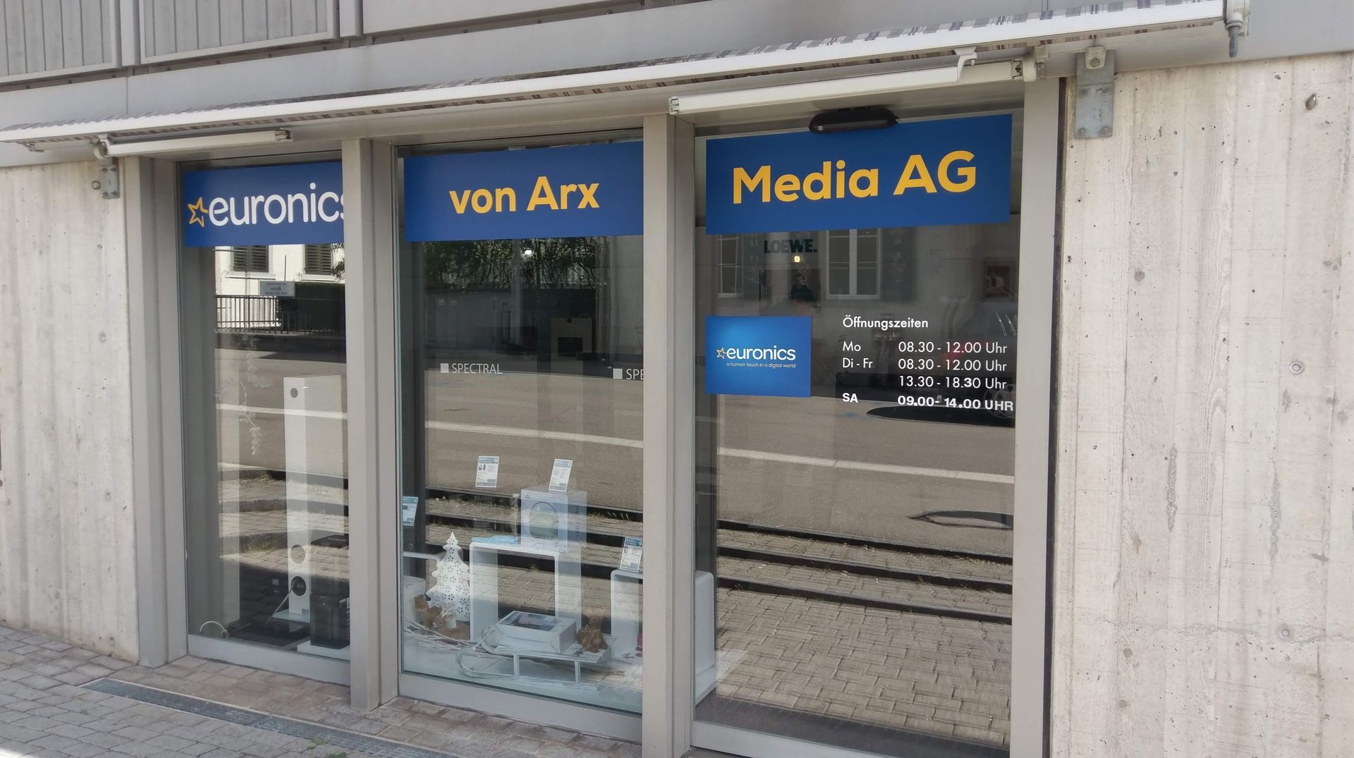 Euronics Zollinger-Geschäftsfront mit blauen Schildern und gläsernem Eingang an einem Kopfsteinpflasterweg
