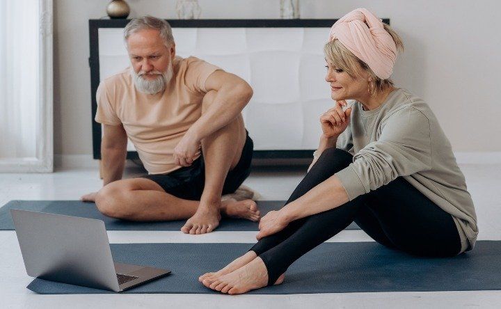 Man and woman sitting on exercise mats attending an online exercise class.