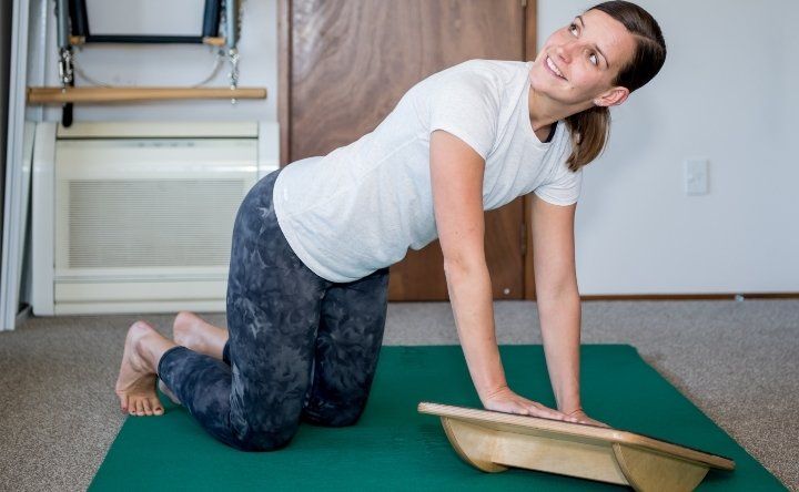 Woman in Pilate studio on hands and knees, with hands on a Spring Movement Mini Balance Board.