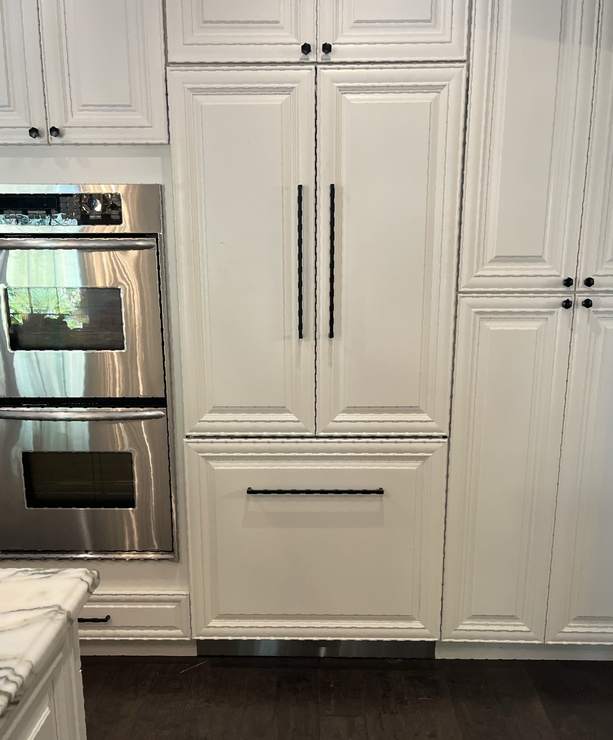 White kitchen cabinetry features a stainless-steel double oven next to a matching paneled refrigerator and bottom freezer.