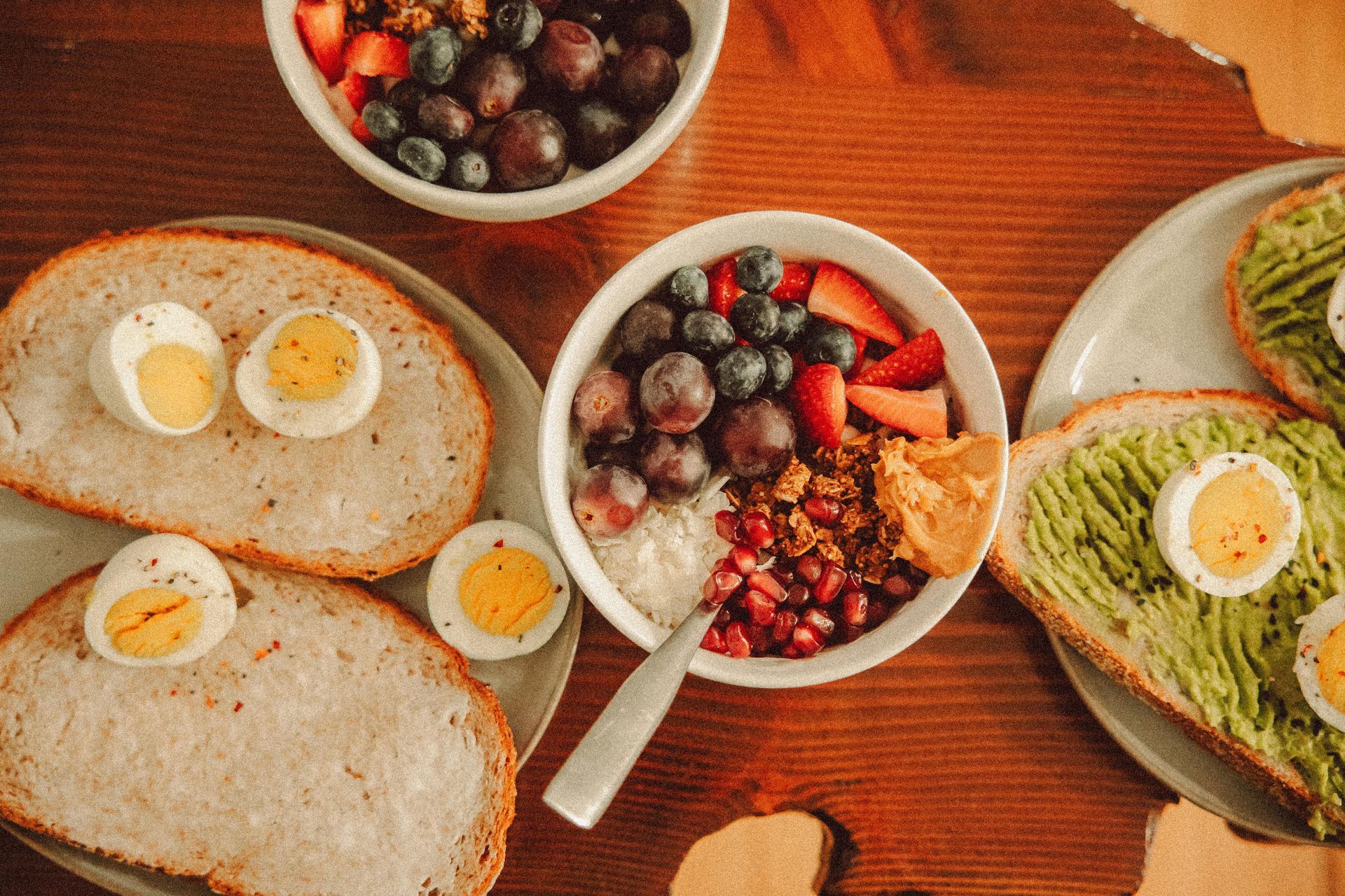 Overhead view of toast, avocado, and berry bowls on a wooden table
