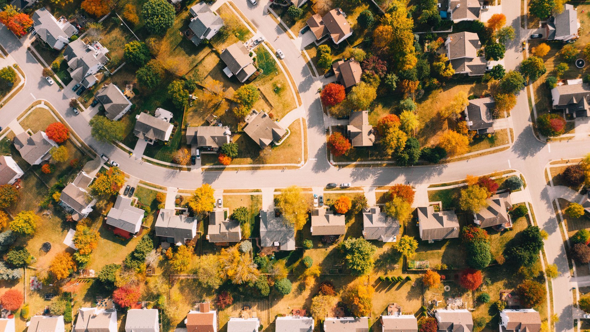 Aerial view of a suburban neighborhood with tree-lined streets, houses, and autumn-colored trees