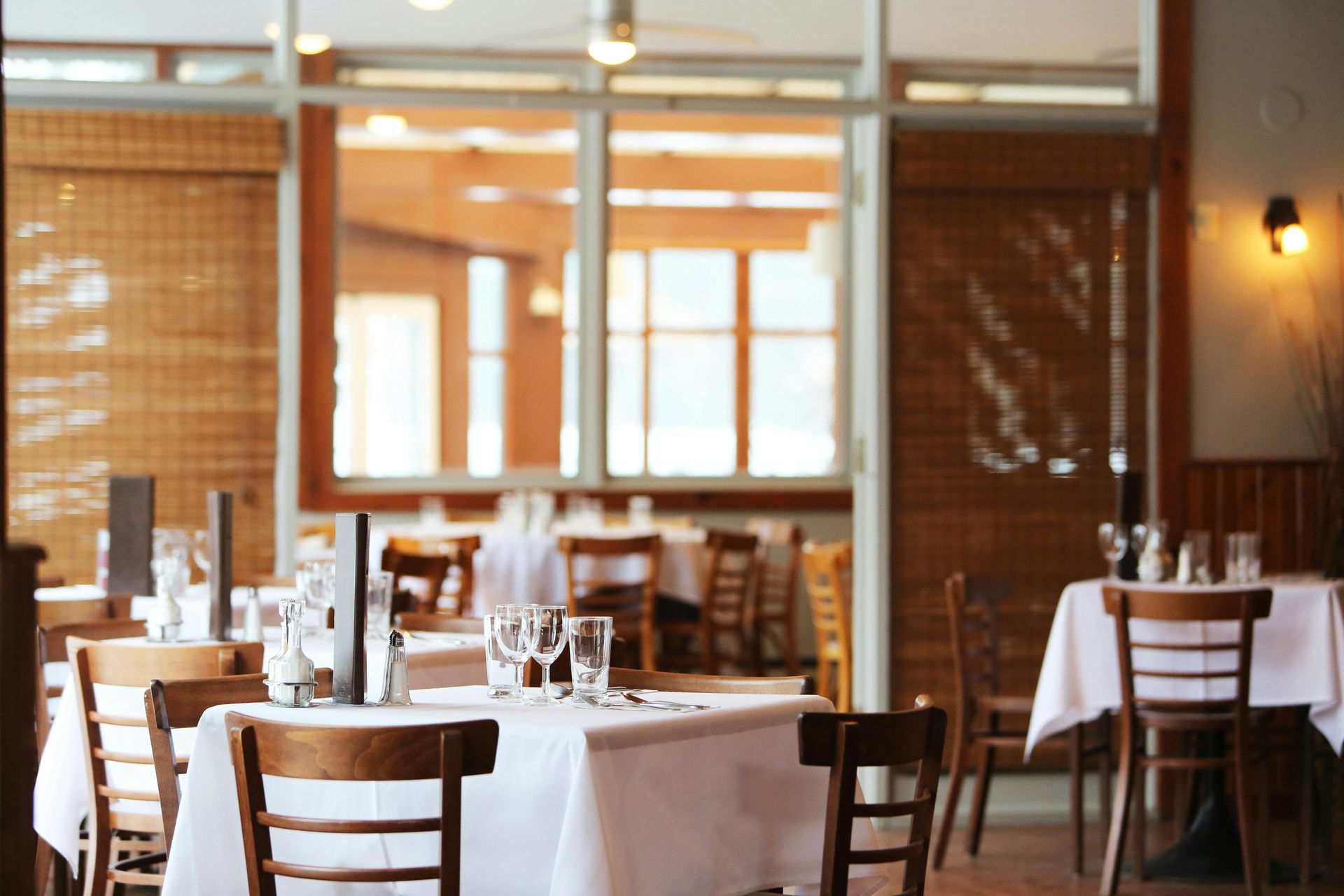 Empty restaurant dining room with white tablecloths, wooden chairs, and warm ambient lighting