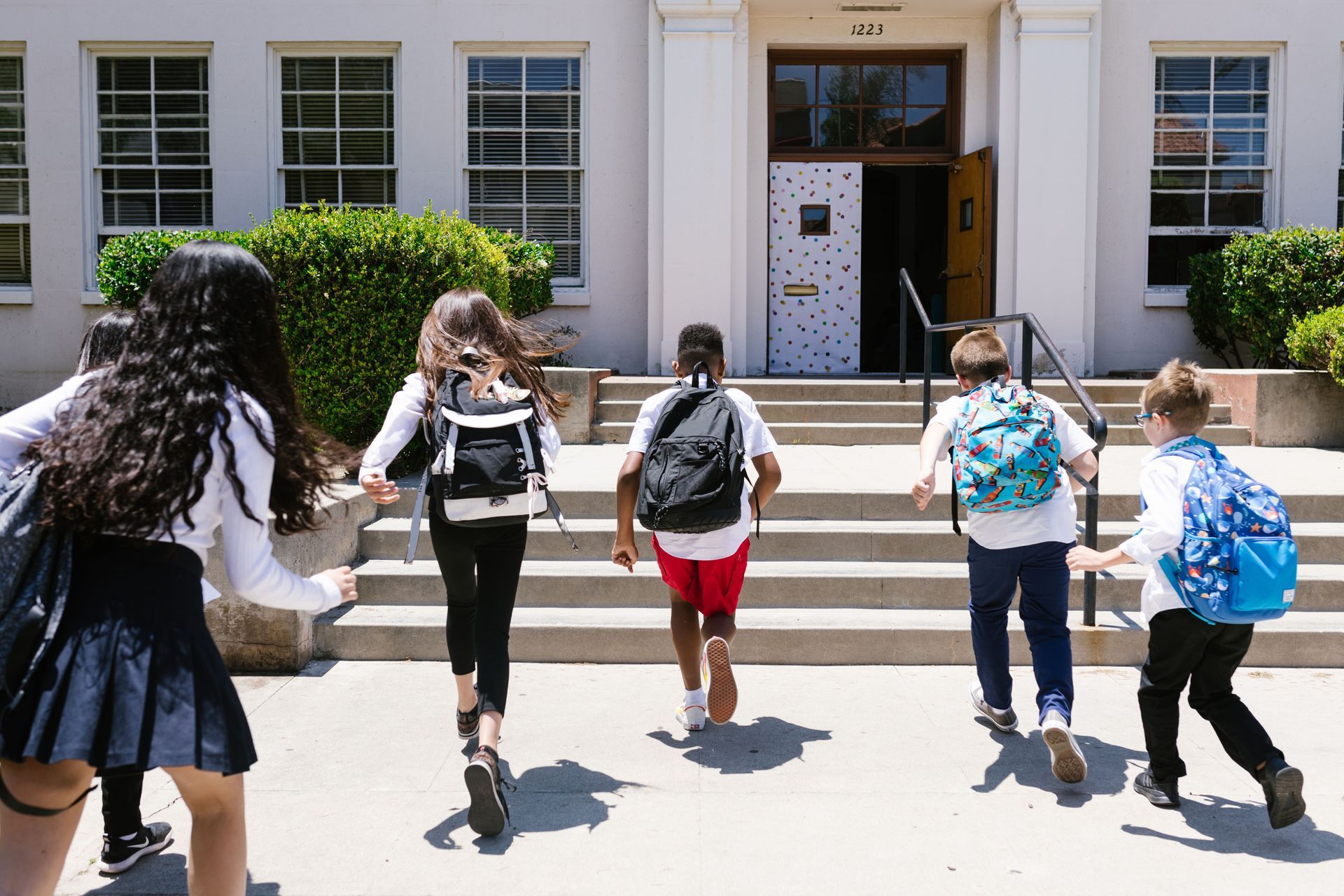Students with backpacks walking toward a school entrance on a sunny day