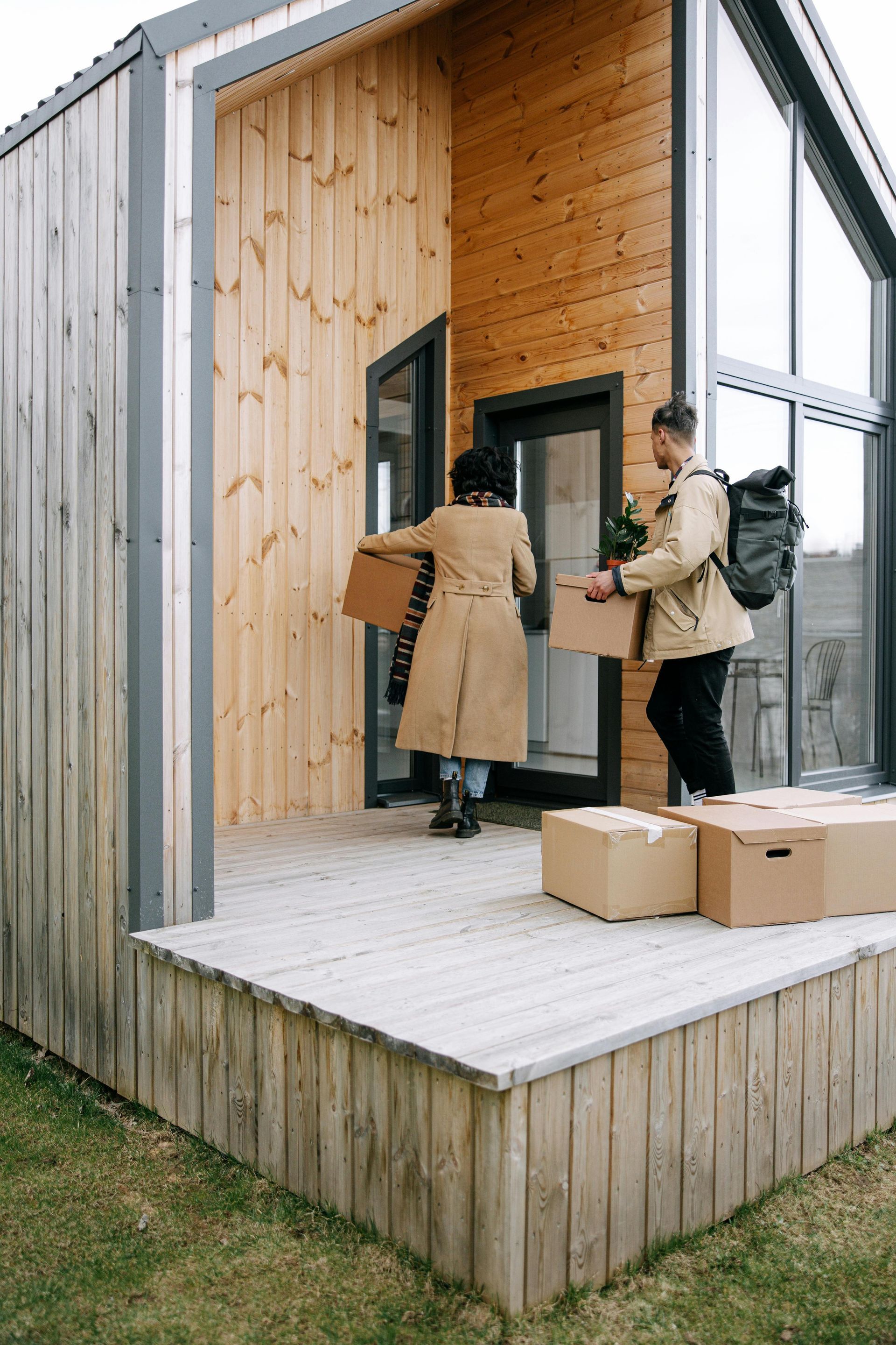 Two people carrying boxes into a small wooden cabin porch