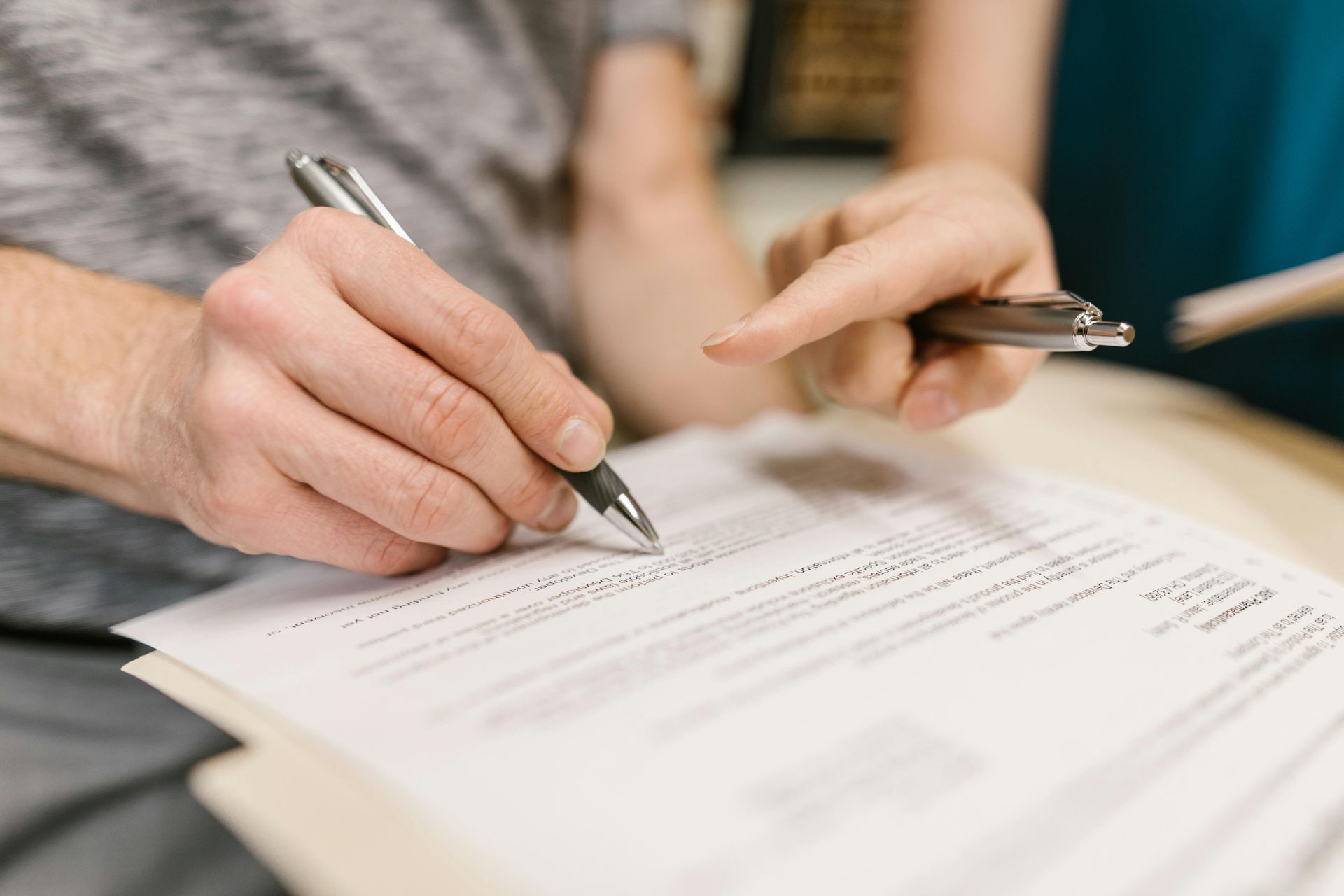 Two people pointing to and signing a document on a clipboard.