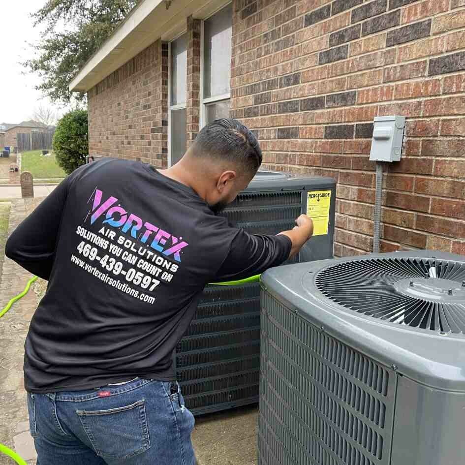HVAC technician inspecting an air conditioning unit outside a brick building.